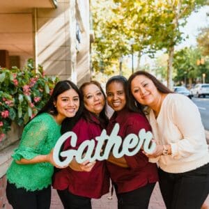 people smiling and holding gather sign