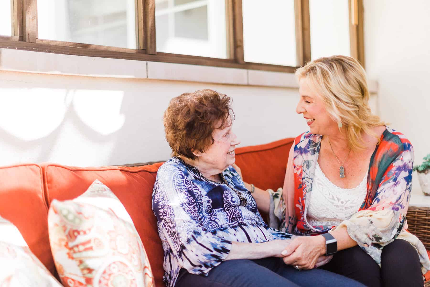 elderly woman and adult woman sitting together holding hands and smiling
