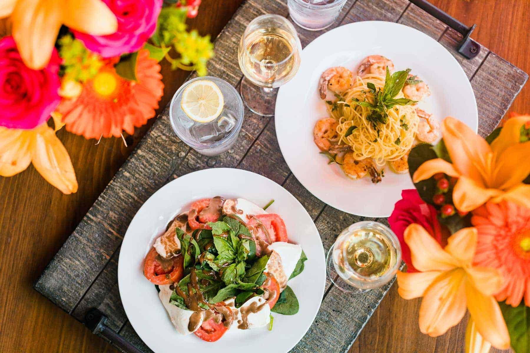 caprese salad, pasta dish with shrimp, glasses of wine and flowers