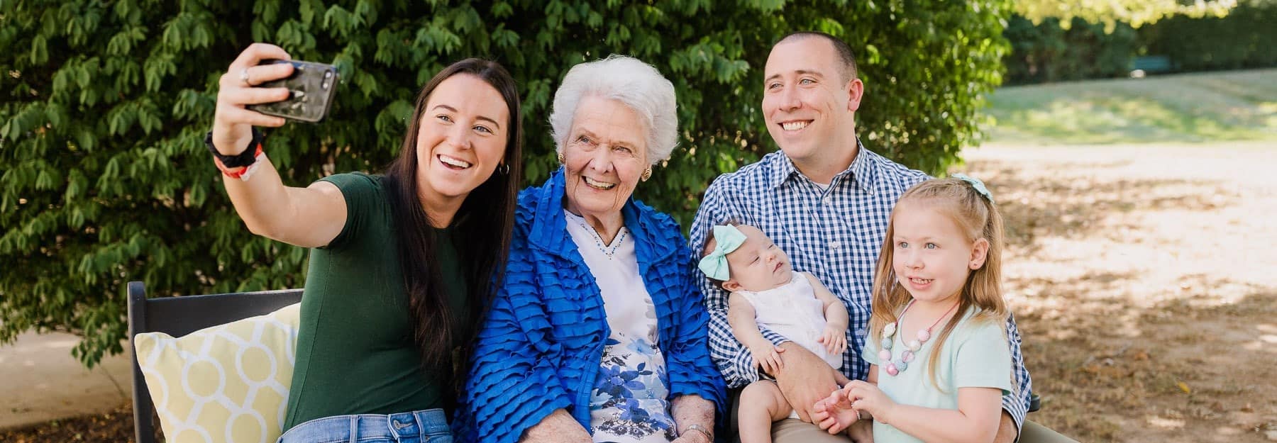 parents and young children smile for photo on cell phone with elderly resident woman