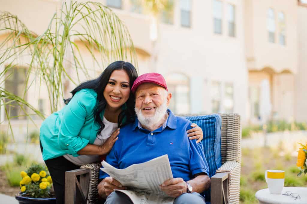 woman hugging old man sitting down with newspaper