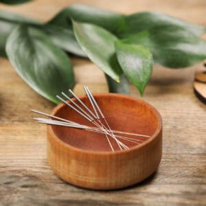 Bowl with acupuncture needles on wooden table